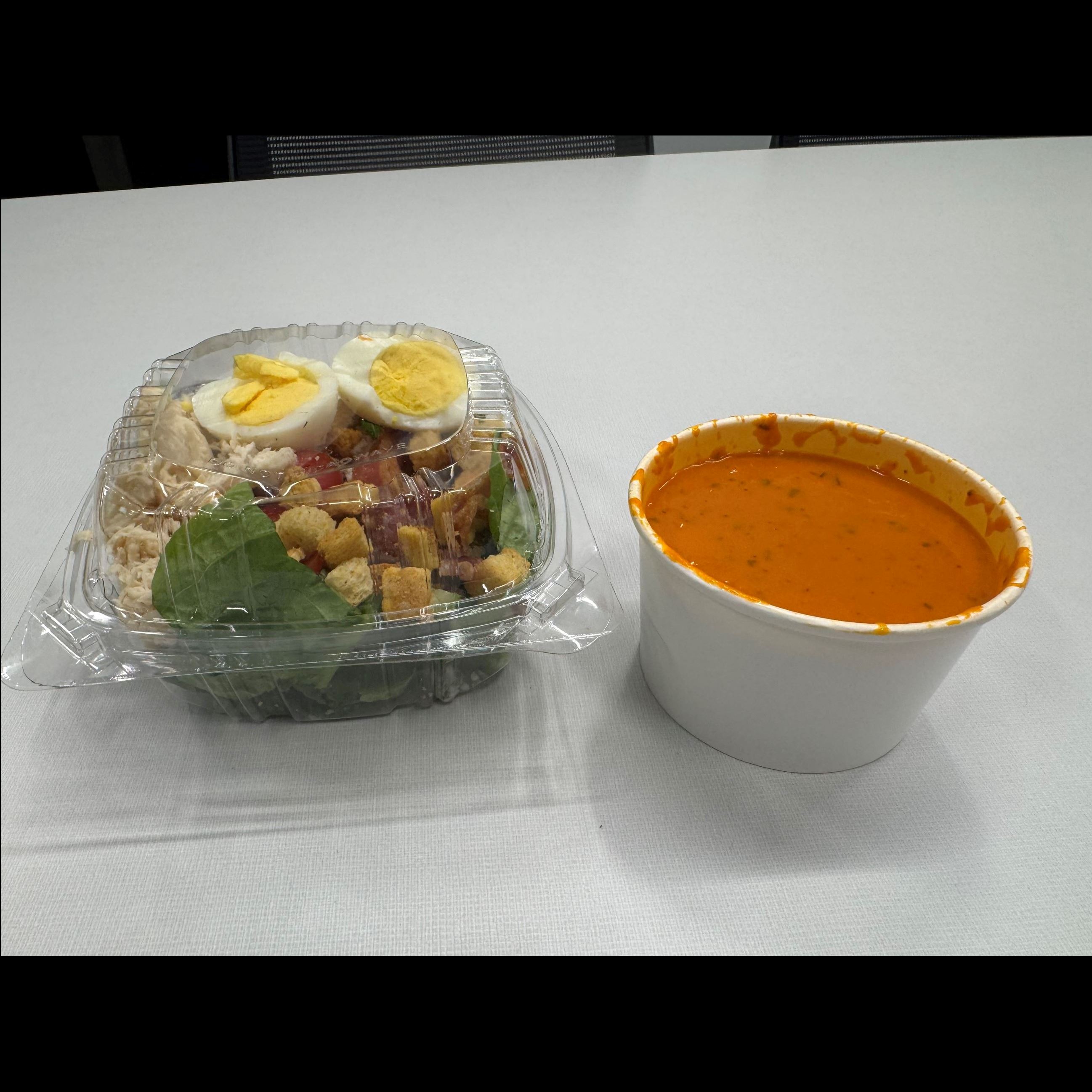 plastic container with salad and hardboiled eggs and a cup of soup